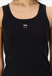 Svart ribbet tank-top med rund halslinning og et lite hvitt logodesign på brystet. Myk tekstur og figurnær passform.