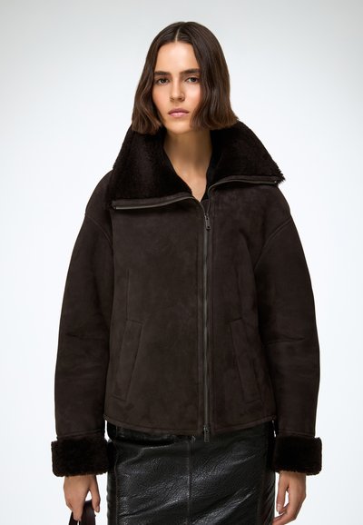 Brązowa kurtka zamszowa z puszystym czarnym kołnierzem, zamkiem błyskawicznym i bocznymi kieszeniami. Teksturowane wykończenie z szerokimi rękawami i futrzanymi mankietami.