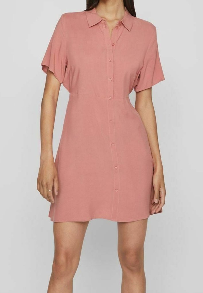 Abito a maniche corte, con bottoni, di un delicato tono rosa. Tessuto morbido, corpetto aderente, gonna fluida e un classico design del colletto.
