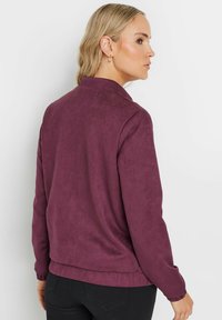 Giacca in finta suede bordeaux con colletto, polsini elasticizzati e vestibilità rilassata, caratterizzata da una texture liscia e un design minimalista.