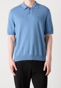 Polo à manches courtes bleu clair avec col en maille plate, patte à deux boutons, et ourlet et manches côtelés. Présente un logo discret.