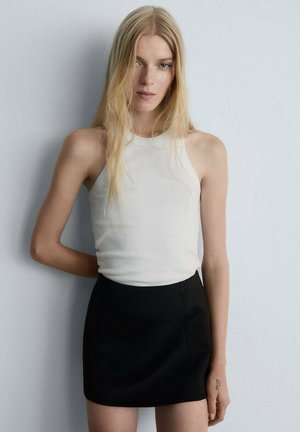 Top halter bianco a costine abbinato a una mini gonna nera. Il tessuto appare liscio, aderente e presenta cuciture visibili lungo la gonna.