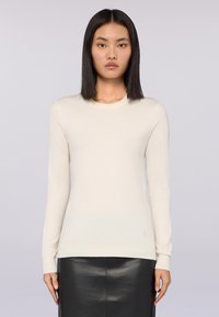 Suéter de manga larga color beige claro, con cuello redondo acanalado, textura suave y silueta ajustada, combinado con una falda de cuero negra.