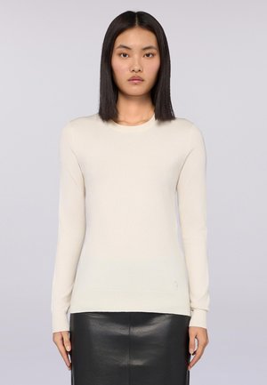 Pull-over beige clair à manches longues, col rond côtelé, texture douce et silhouette ajustée, associé à une jupe en cuir noire.