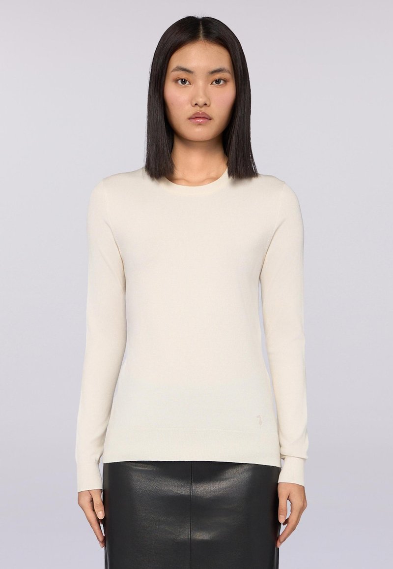 Suéter de manga larga color beige claro, con cuello redondo acanalado, textura suave y silueta ajustada, combinado con una falda de cuero negra.
