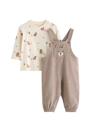 Kremfarget langærmet skjorte med print af bjørn og træ, kombineret med taupe overalls med en lomme formet som en bjørneansigt og ører på stropperne.