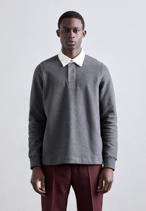 Sweatshirt gris avec un col boutonné blanc, des manches longues et un logo brodé à l'ourlet. Le tissu semble doux avec une texture subtile.