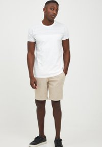 T-shirt blanche à manches courtes avec des panneaux en maille texturée, associée à un short beige et des baskets noires, offrant une coupe décontractée et un design simple.