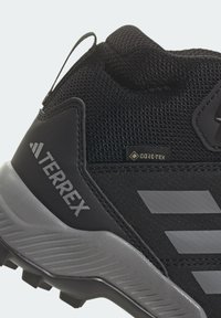 Zapato de senderismo negro con parte superior de malla texturizada, detalles de goma gris, talón reforzado y etiqueta GORE-TEX para resistencia al agua.