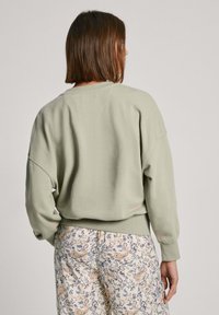 Lichtgroene, oversized sweatshirt met een ronde hals en raglanmouwen, gecombineerd met gemusterde, lichtgekleurde broek.