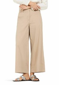 Beige, wide-legged trousers made of lightweight fabric, featuring a smooth texture and front pockets. Paired with metallic silver sandals.