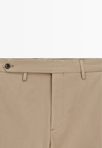 Pantaloni beige con un morbido tessuto in misto cotone, dotati di chiusura a bottone, passanti per cintura e design affusolato. Nessun motivo o dettaglio visibile.