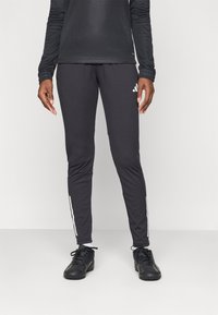 Svarte treningbukser med hvite sidekrager, innsvingt design, laget av elastisk stoff, kombinert med svarte treningssko og en langermet topp.