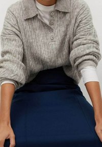 Maglione grigio chiaro a maglia traforata con collo e tre bottoni, abbinato a una gonna blu fitted. Tessuto morbido e vestibilità rilassata.