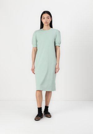 Mintgroene katoenen jurk met korte pofmouwen, knielange snit en een ontspannen pasvorm. Gecombineerd met zwarte sokken en schoenen met luipaardprint.
