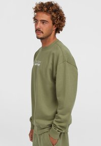 Oliven grøn sweatshirt med ribbet rund hals og manchetter, prydet med hvid tekst på fronten. Fremstillet af blødt, tekstureret stof.