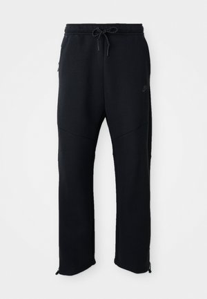 Black athletic pants with elastic waistband and drawstring, feature side pockets, tapered legs, and zippers at the ankles. Smooth texture.