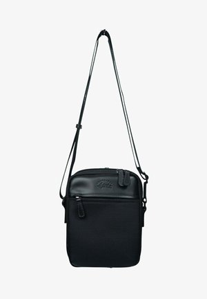 Sac bandoulière noir avec un corps en tissu texturé et des accents en cuir lisse, un compartiment principal zippé et une bandoulière réglable.