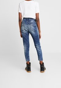 Höga blå jeans med en bleknad tvätt, avsmalnande ben, bakfickor och sydda detaljer, kombinerade med svarta ankelboots.