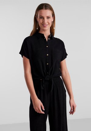 Camicia nera con bottoni, realizzata in un tessuto morbido, con maniche corte, due tasche sul petto e un dettaglio annodato in vita.