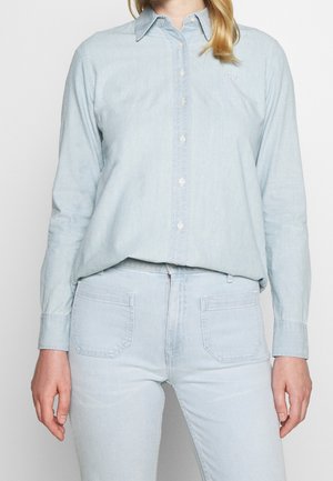 Ljusblå denimskjorta med knäppning framtill, krage och långa ärmar. Har subtil logobrodyr på bröstet och en avslappnad passform.