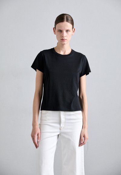 T-shirt noir à manches courtes en coton, avec un col rond et un ourlet droit, associé à un pantalon blanc à jambes larges.