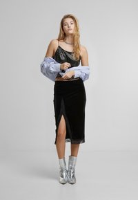 Juodas aksominis sijonas su nėrinių apdaila ir šonine plyšio, derinamas su blizgia juoda top ir oversized mėlynomis dryžuotomis marškinėliais. Sidabriniai kulkšnies aukštakulniai.