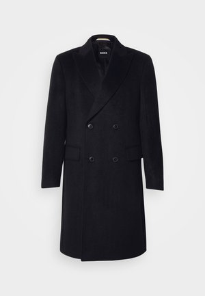Tweekleurige zwarte wollen jas met notch-lapels, twee voorzakken en twee knopen, ontworpen met een rechte silhoutte.