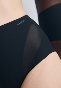 Sorte høytrukne truser med en transparent sidepanelet og Calvin Klein-logo på midjebåndet, som viser glatt stoff og sømløst design.