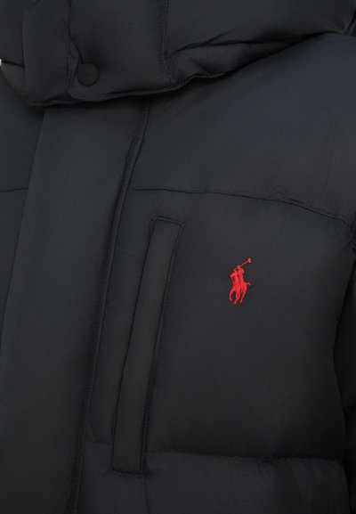 Juodas pūkuotas švarkas su gobtuvu, su priekinėmis kišenėmis ir mažuoju raudonu siuvinėtu logotipu ant krūtinės. Pagamintas iš lygaus, patvaraus medžiagos.