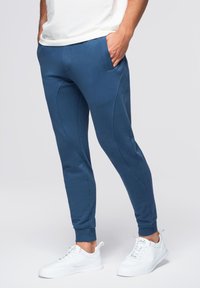 Marineblauwe trainingsbroek met een slim fit ontwerp, voorzien van zijzakken en textuuraccenten langs de naden. Gedragen met witte sneakers.