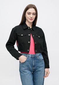 Mustast lühendatud teksatagi, millel on nööpkinnitused, kaks rinnataskut ja terav krae, kantud roosa topi kohal, siniste teksadega kokku pandud.