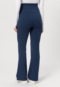 Pantalones acampanados de color azul marino hechos de tela elástica con una cintura alta, combinados con zapatillas blancas, mostrando una textura suave.