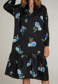 Robe noire à fleurs avec des roses bleues et des accents verts ; présente un décolleté en V, des manches longues et un ourlet volé. Fabriquée en tissu lisse.