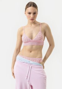 Brassière en dentelle rose clair avec des bonnets triangles et des fines bretelles, associée à un pantalon de jogging rose assorti avec une taille bleu pâle.