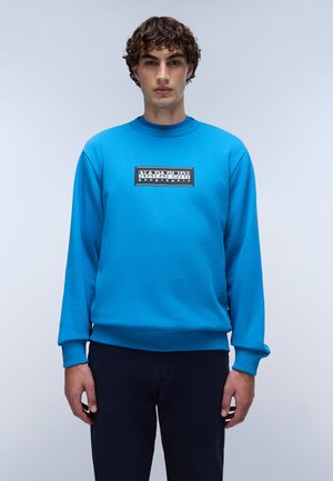 Blaues Sweatshirt aus weichem Stoff, mit Rundhalsausschnitt, gerippten Bündchen und einem kontrastierenden schwarzen Logopatch auf der Vorderseite.