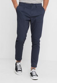 Granatowe spodnie o dopasowanym kroju z bocznymi kieszeniami. Wykonane z gładkiej tkaniny, z zapięciem na guzik, o długości do kostek.