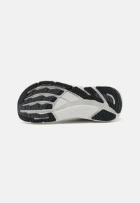 Semelle de chaussure au design courbé, avec une base principalement blanche et des motifs de caoutchouc noir texturé, ainsi que des rainures de flexion pour une meilleure adhérence.
