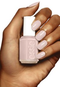 Vernis à ongles rose clair dans un flacon en verre carré avec un capuchon blanc, tenu par une main présentant des ongles manucurés rose clair assortis.