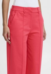 Korallenrote weite Hosen mit vorderen Taschen, gefältelten Details, einer glatten Textur und einem mittelhohen Bund.