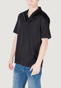 Polo shirt nero a maniche corte con colletto angolato unico, realizzato in tessuto liscio, abbinato a jeans in denim blu.