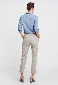 Chemise en denim bleu clair à manches retroussées, associée à un pantalon beige clair fuselé et des chaussures à talons blocs à motifs. Vue de dos.