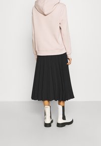 Roze capuchontrui gecombineerd met een zwarte geplooide rok en witte enkellaarsjes met zwarte zijpanelen. Gladde stof en gestructureerd ontwerp.