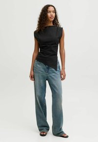 Sort ærmeløs top med høj hals og asymmetrisk kant, parret med løse lyse jeans for en afslappet silhuet.