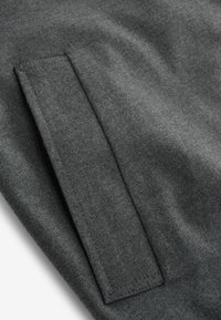 Grau meliertes Wollmischgewebe mit glatter Textur; verfügt über ein rechteckiges, genähtes Taschendetail. Einfaches, minimalistisches Design.