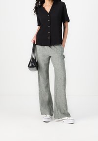 Černá košile na knoflíky s krátkým rukávem, spárovaná se světlými zelenými lněnými širokými kalhotami. Černá kabelka a bílé tenisky.