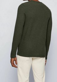 Olivgrön långärmad skjorta med rundad halsringning, ribbade ärmslut och en mjuk textur. Stickade detaljer längs sömmarna.