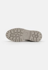 Vaaleanharmaa kuminen kengänpohja, jossa on tekstuurinen pohja, syviä uria ja kuusikulmaisia muotoja, jotka tarjoavat pitoa ja kestävyyttä.