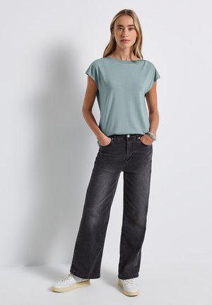 Lichtblauwe T-shirt met korte mouwen in een ontspannen pasvorm, gecombineerd met hoge zwarte wijde pijpen jeans en witte sneakers.