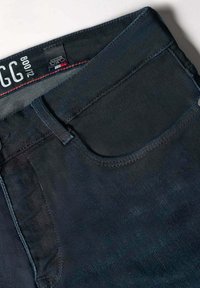 Jeans de mezclilla azul oscuro con un diseño clásico de cinco bolsillos, costuras en contraste y una textura sutil. La etiqueta muestra el nombre de la marca y la talla.